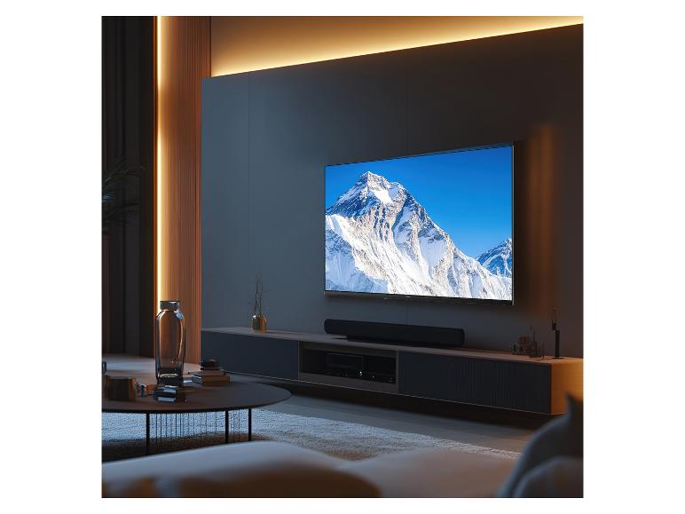 Großer Fernseher an der Wand mit Soundbar und Mediengerät in einem modernen Wohnzimmer.