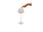 Weiße Tischlampe mit plissiertem Schirm, von einem Finger eingeschaltet.