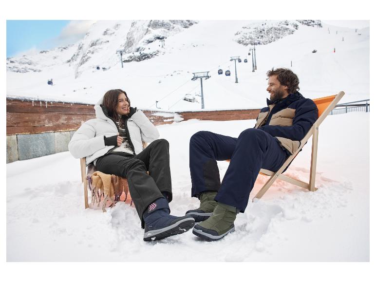 Zwei Personen entspannen in Liegestühlen im Schnee, tragen Skijacken und -hosen.