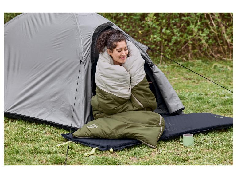 Frau in einem zweifarbigen Schlafsack, sitzt in einem Zelt mit Isomatte und Tasse.