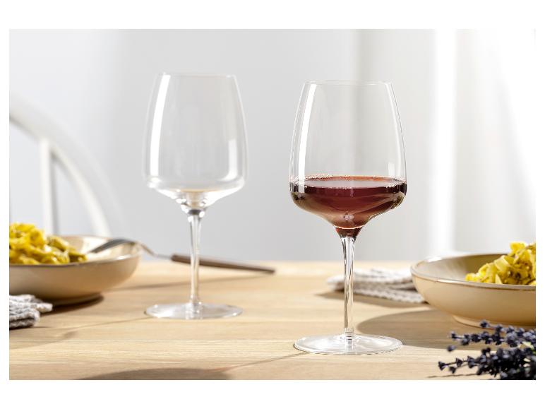 Zwei Weingläser, eines mit Rotwein gefüllt, auf einem Holztisch mit Nudelgerichten.