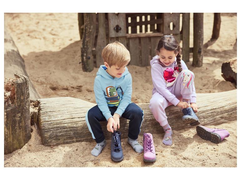 Zwei Kinder ziehen Stiefel auf einem Holzstamm auf einem Sandspielplatz an.