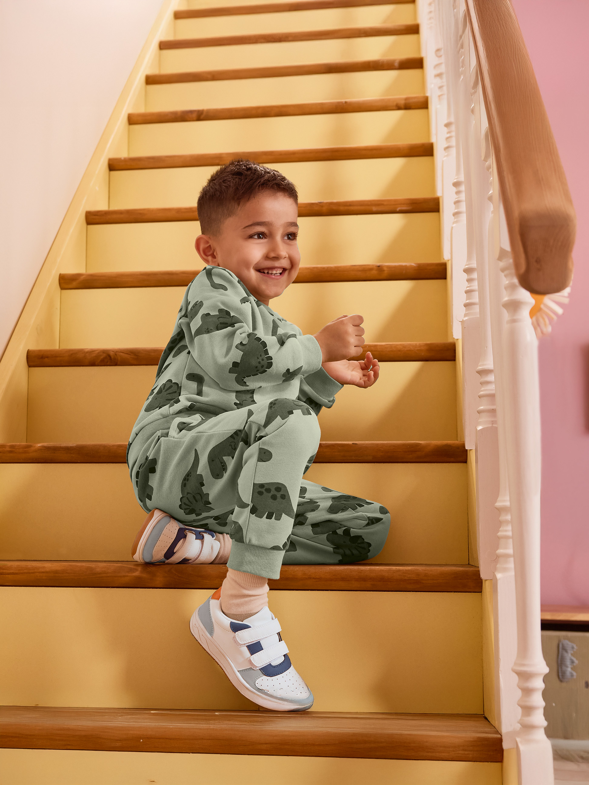Junge im grünen Dinosaurier-Pyjama sitzt lächelnd auf der Treppe.
