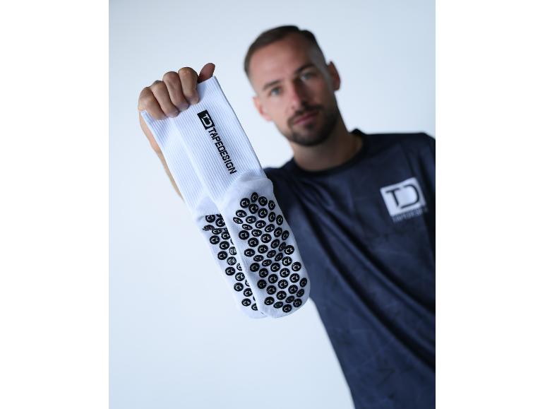 Mann hält weiße TAPEDESIGN Sportsocken mit Anti-Rutsch-Noppen.