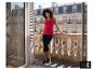 Eine lächelnde Frau in einem roten ESMARA® Top und schwarzen Leggings auf einem Balkon. [KI-generiertes Bild]