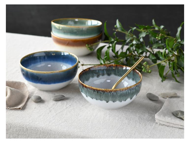 Keramikschalen in Blau, Grün und Braun mit Goldrand auf einer Leinentischdecke.
