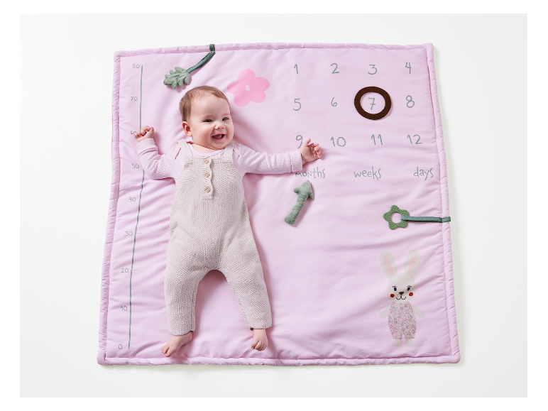 Ein Baby liegt auf einer rosa Spieldecke mit Höhenmesser und Spielzeug.