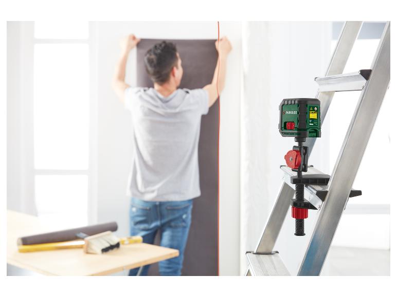 Mann benutzt eine Parkside Laserwasserwaage, montiert auf einer Leiter, um Tapeten anzubringen.