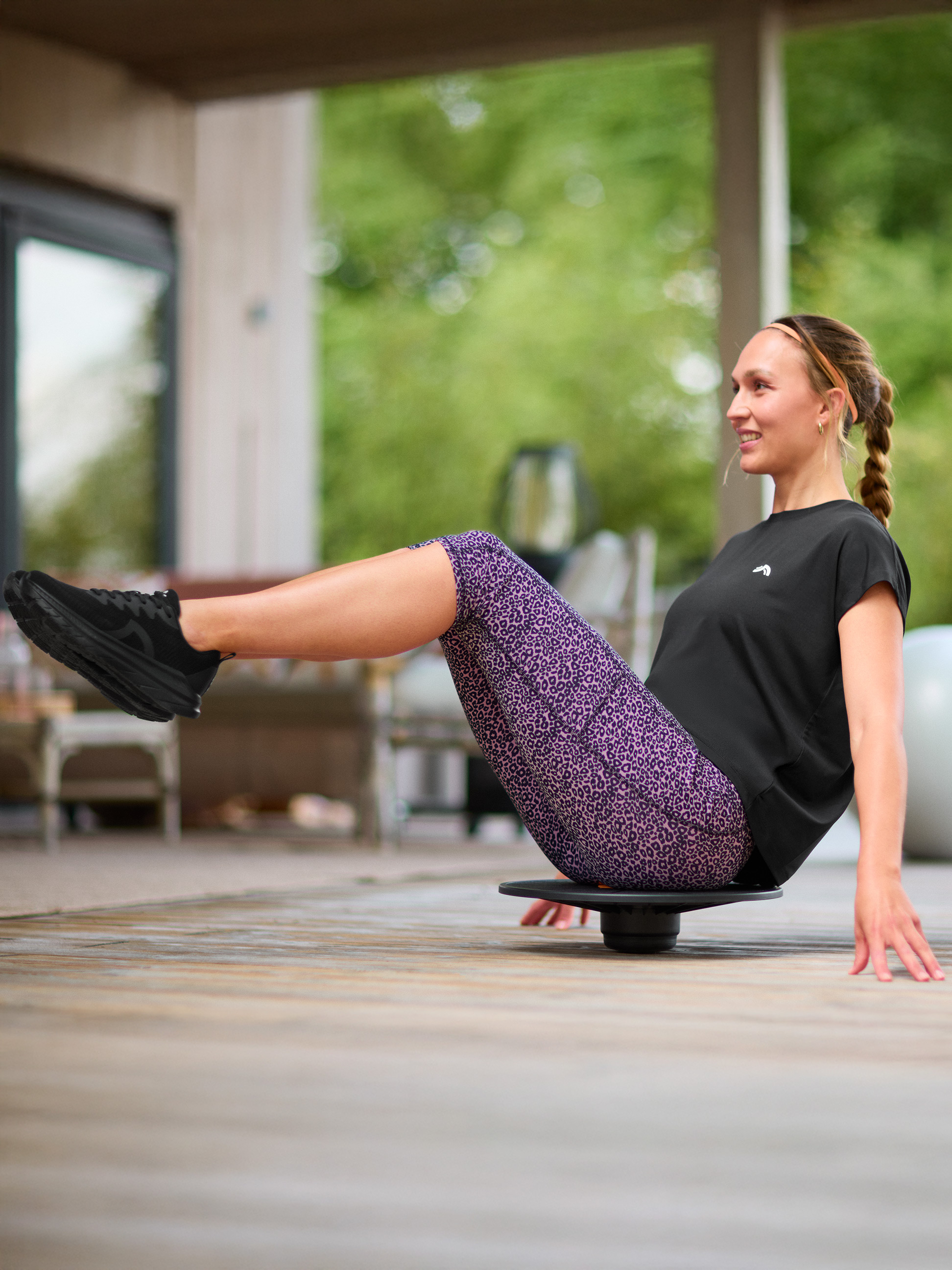 Frau trainiert Gleichgewicht auf einem Balance Board, trägt ein schwarzes T-Shirt und Leggings mit Leopardenmuster.