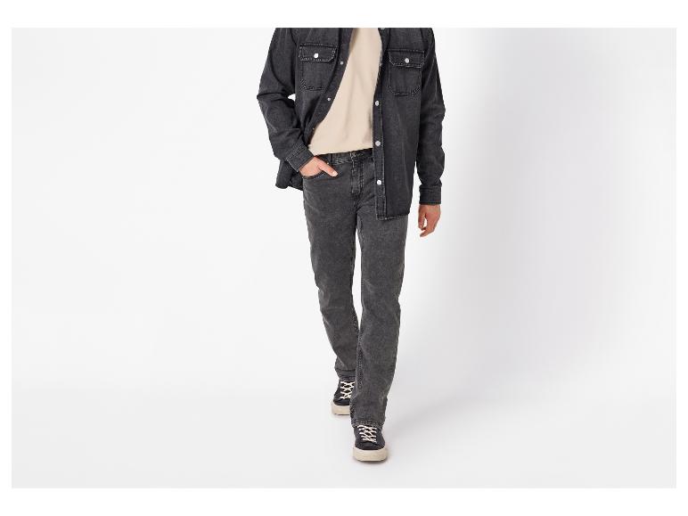 Mann in schwarzem Jeanshemd, beigem T-Shirt und dunkelgrauen Jeans geht vorwärts.