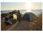 Paar beim Campen am Meer mit Zelten und einem CRIVIT Schlafsack bei Sonnenuntergang.