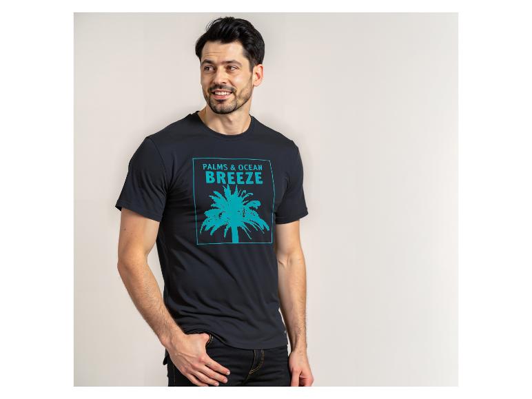 Mann in schwarzem T-Shirt mit türkisfarbenem Palmen- und „PALMS & OCEAN BREEZE“-Aufdruck.