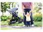 Ein Baby macht seine ersten Schritte, gehalten von einem Mann, im Hintergrund ein Kinderwagen.