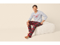 Mann sitzt auf einem Pouf, trägt ein graues Sweatshirt mit „LETS STAY IN BED (FOREVER)“ und rot karierte Pyjamahose.