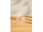 Klares stielloses Glas auf einem hellen Holztisch mit subtilen Wandschatten.