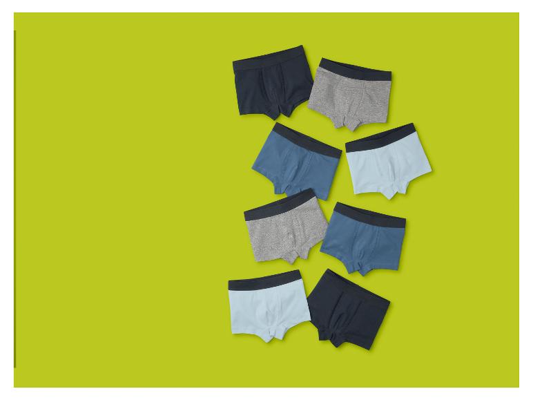 Acht Jungen-Boxershorts in verschiedenen Blau- und Grautönen auf limettengrünem Hintergrund.