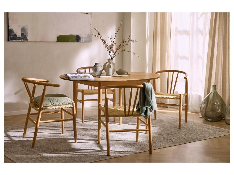 Runder Holzesstisch mit vier Stühlen, einem Teppich und einer Vase mit Blumen.