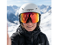 Person in weißem Skihelm und reflektierender Skibrille, schwarzer Skijacke, verschneite Berge im Hintergrund.