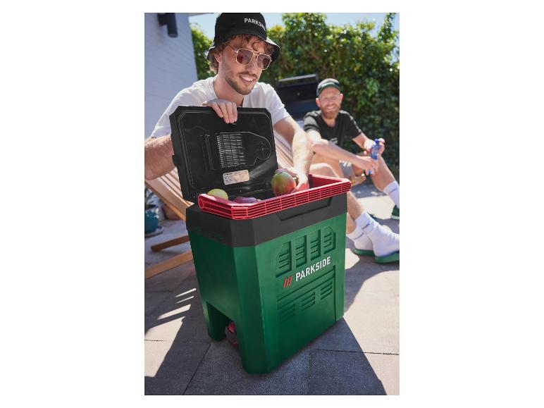 Zwei Männer im Freien, einer öffnet eine grün-schwarze Kühlbox mit Obst darin.