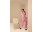Eine Frau in einer rosa Weste und einer weiten Hose posiert in einem minimalistischen Studio.