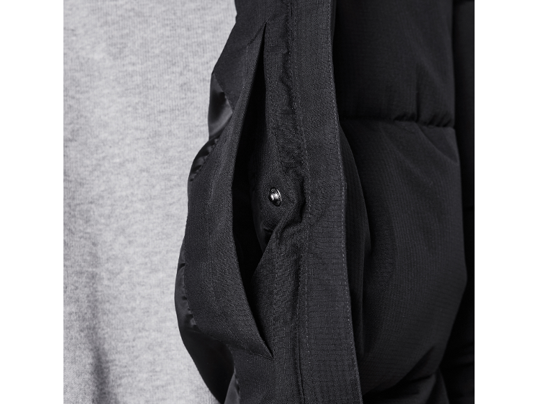 Detail einer schwarzen Steppjacke mit Seitentasche und Druckknopf.