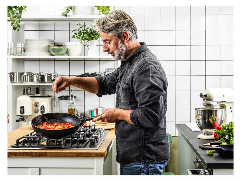Mann kocht mit einem Wok auf einem Gasherd in einer modernen Küche mit Küchengeräten