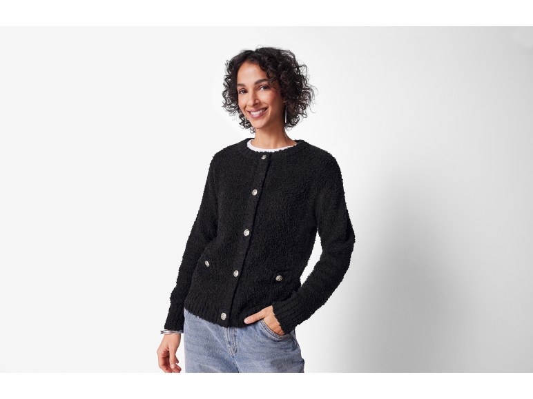 Lächelnde Frau in schwarzer strukturierter Strickjacke und Jeans, Hand in der Tasche.