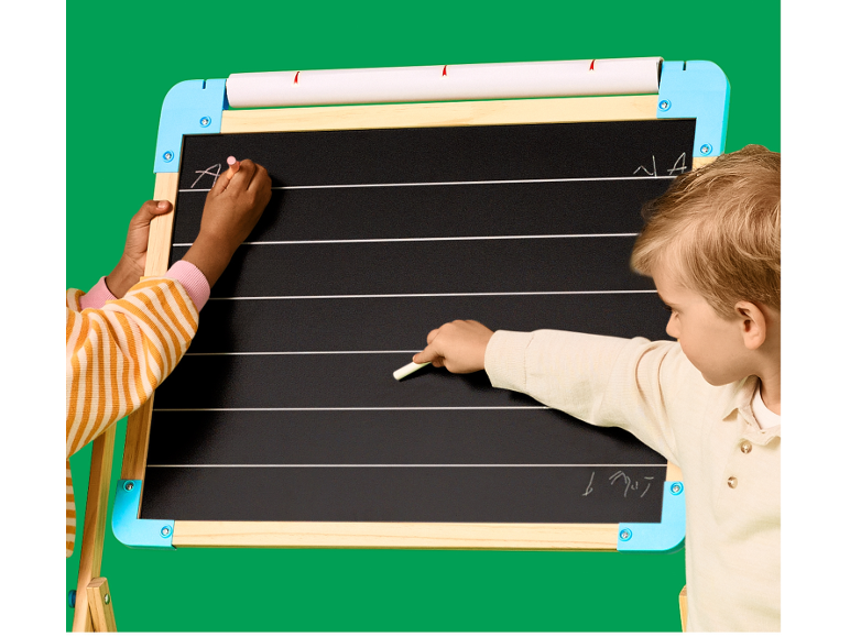 Zwei Kinder schreiben mit Kreide auf einer Tafel mit Linien zum Schreibenlernen.