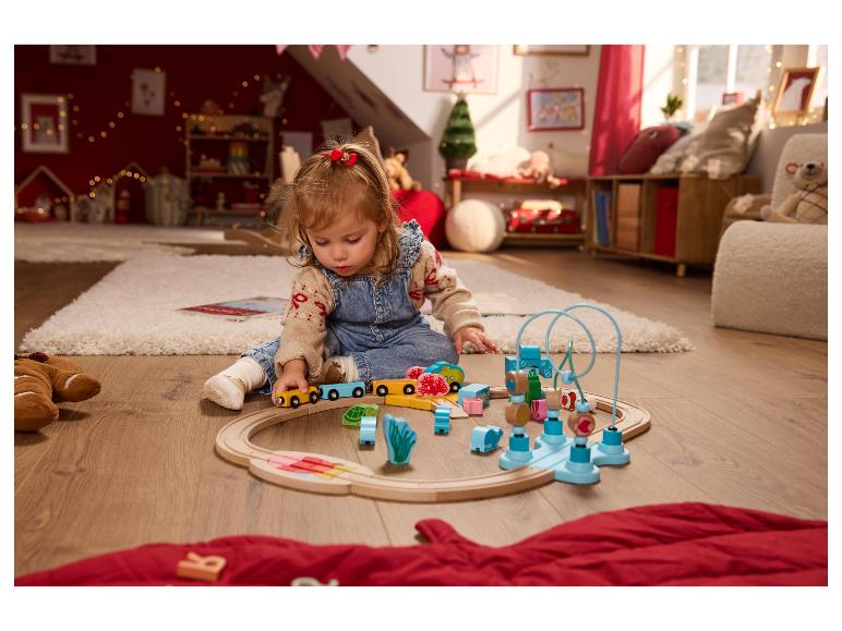 Kleinkind spielt mit einer Holzeisenbahn und anderem bunten Holzspielzeug auf einem Teppich.