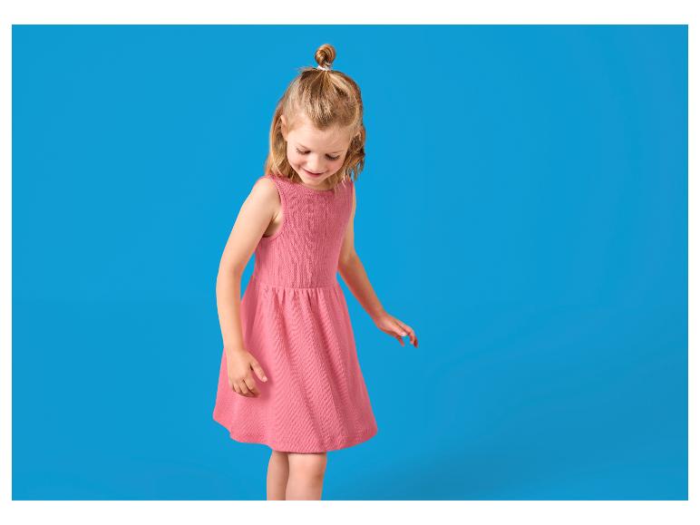 Kleines Mädchen in rosa Kleid mit Dutt, schaut nach unten.