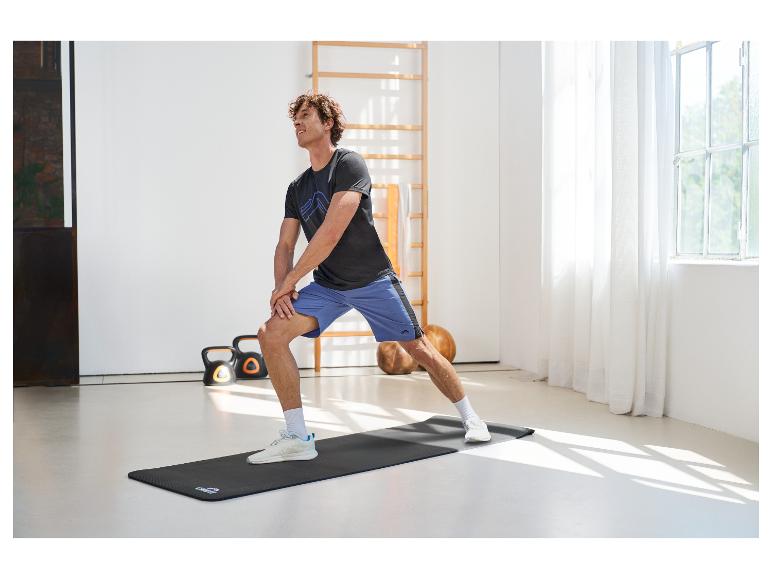 Mann macht Dehnübungen auf einer Fitnessmatte, trägt Sportshirt und Shorts.