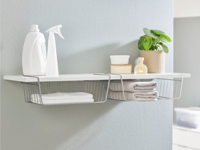 Zwei Metall-Ablagekörbe unter einem weißen Regal mit Handtüchern, Reinigungsmitteln und einer Pflanze.