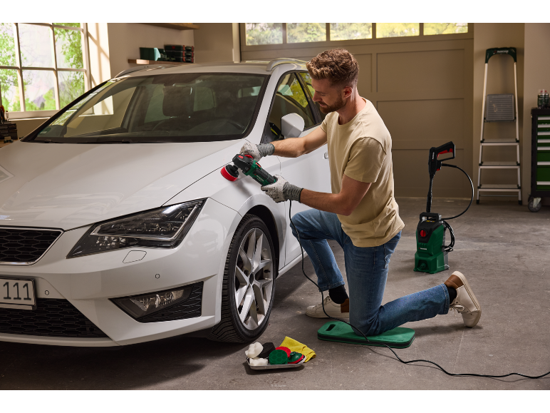 Ein Mann poliert ein weißes Auto mit einer Rotationspoliermaschine in einer Garage.