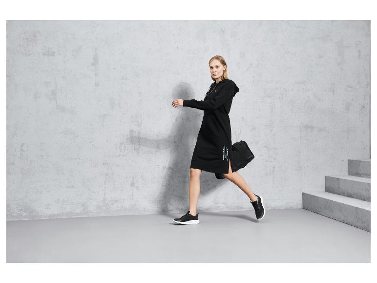 Frau in einem schwarzen Kapuzenkleid und schwarzen Sneakers.