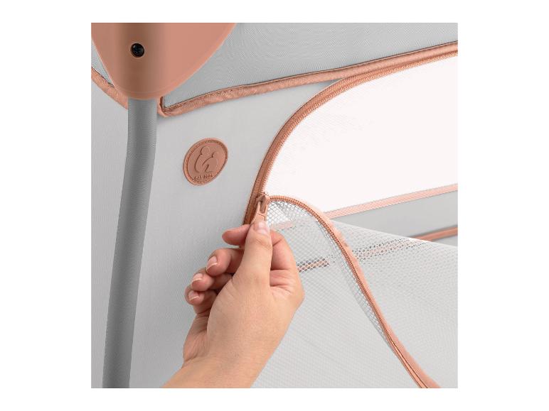 Hand schließt Reißverschluss am Seitennetz eines grauen und rosa Reisebettes