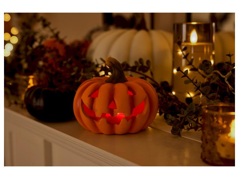 Leuchtender orangefarbener LED-Halloween-Kürbis auf einem dekorierten Kaminsims.