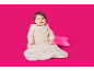 Lächelndes Baby in Bio-Baumwoll-Schlafsack mit Hasen- und Mondmuster, mit einem rosa Kissen.