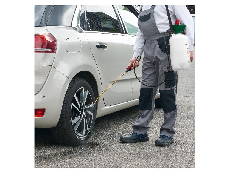 Mann in Arbeitskleidung reinigt Autoreifen mit einem Drucksprüher.