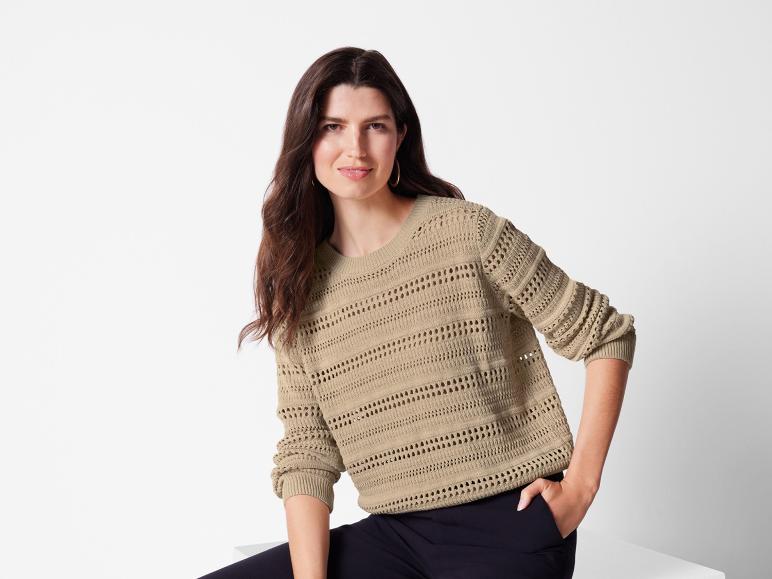 Eine Frau trägt einen beigefarbenen Strickpullover mit durchbrochenen Details.