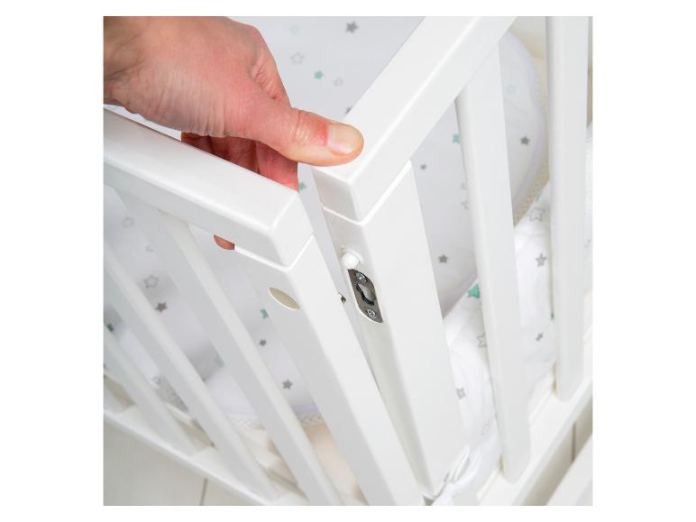 Hand öffnet die Seite eines weißen Babybetts mit Sternen-Bettwäsche.