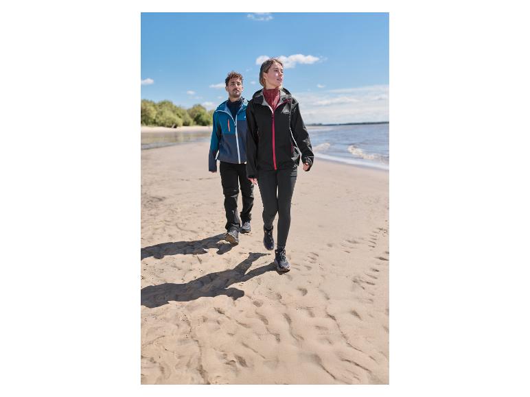 Zwei Personen in Outdoor-Jacken und -Hosen gehen an einem Sandstrand entlang.