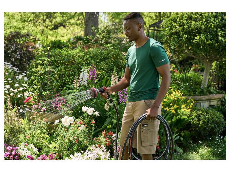 Mann bewässert Blumen in einem Garten mit einem Parkside Gartenschlauch und Sprühpistole.