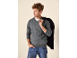 Mann in grauem V-Pullover, Jeans und schwarzer Jacke über der Schulter.