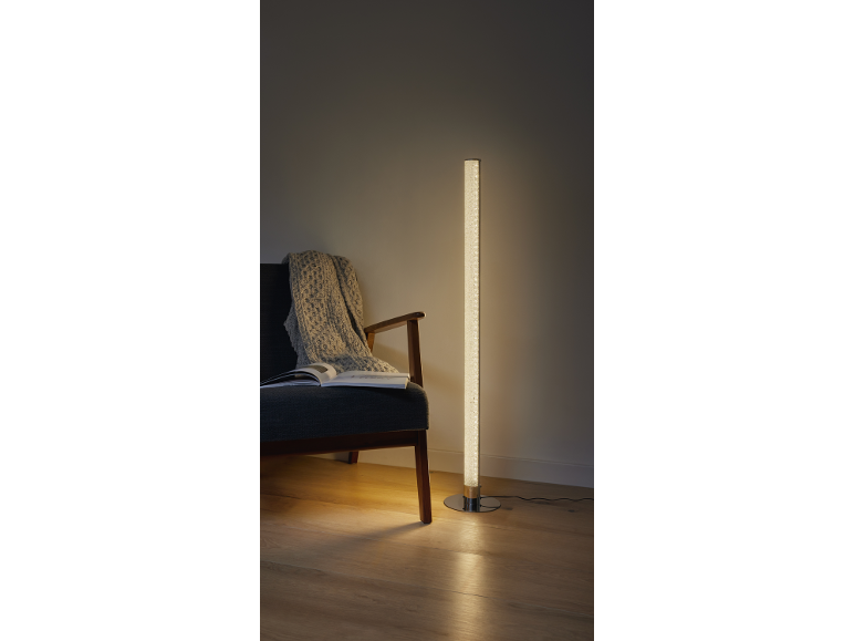 LED-Stehlampe mit Luftblasen neben einem Sessel mit Decke und Buch.