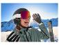 Eine lächelnde Frau mit CRIVIT Skihelm und Premium-selbsttönender Skibrille auf einer sonnigen Piste.