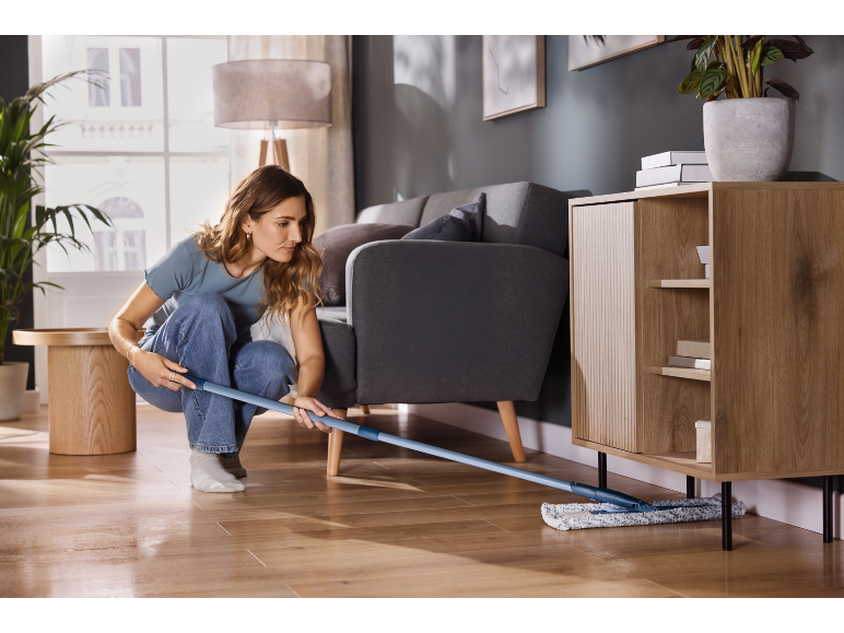 Frau reinigt Holzboden mit einem Flachwischer in einem modernen Wohnzimmer.