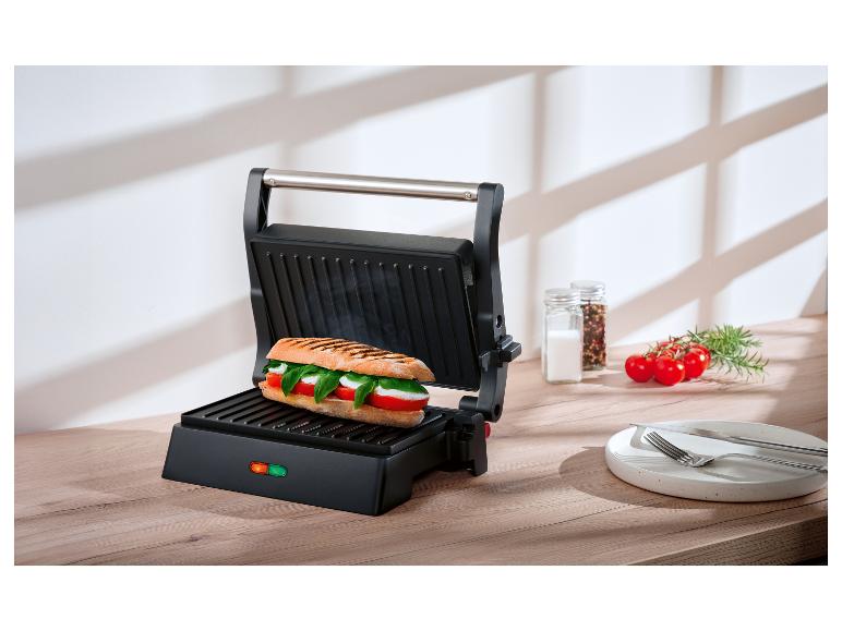Offener Panini-Grill mit Caprese-Sandwich auf Holztisch.