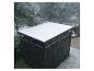 Schwarzer Gartenschuppen mit Schnee auf dem Dach, mit verschneiten Bäumen und Rasen im Hintergrund.
