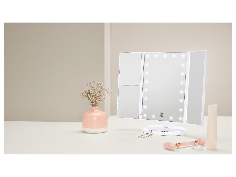 Dreiteiliger Kosmetikspiegel mit LED-Beleuchtung, Vase mit Blumen und Beauty-Produkte auf dem Tisch.