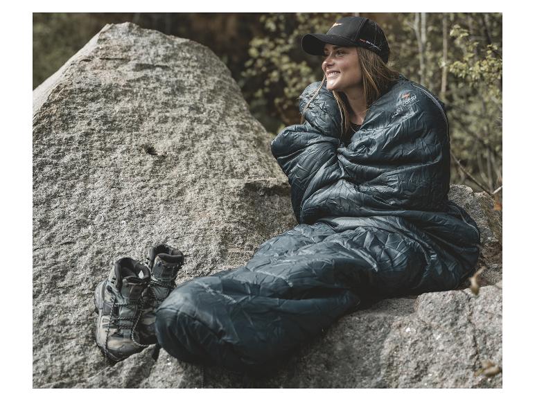 Eine Frau sitzt auf einem Felsen, eingehüllt in einen Easy Camp Schlafsack.
